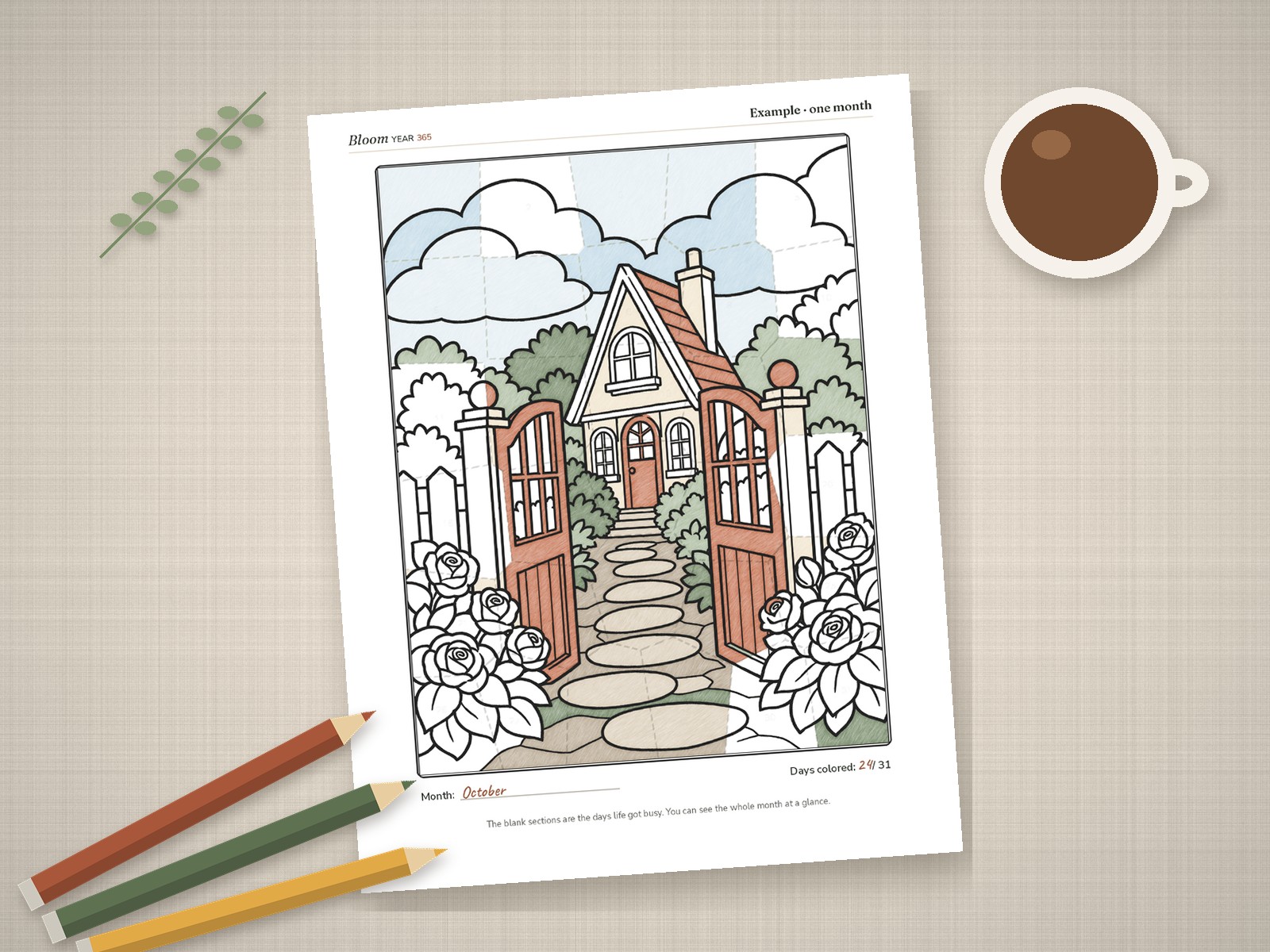 A Bloom Year month page half colored with some day sections blank, on a linen table with colored pencils and a coffee cup in morning light